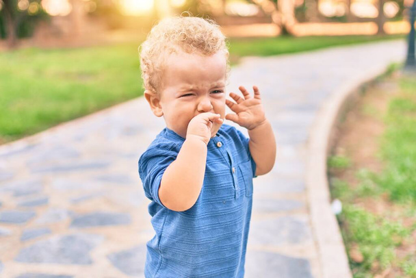 Netter und trauriger kleiner Junge, der an einem sonnigen Tag bei einem Wutanfall im Park weint. Schöne blonde Haare männliches Kleinkind frustriert mit Tränen im Gesicht im Freien - Foto, Bild
