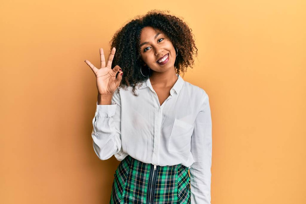 Gyönyörű afro-amerikai nő afro haj visel tudós szoknya mosolyogva pozitív csinál rendben jel kézzel és ujjakkal. sikeres kifejezés.  - Fotó, kép