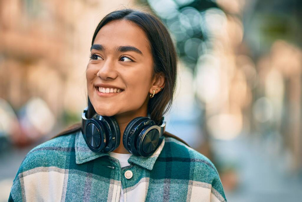 Joven chica latina sonriendo feliz usando auriculares en la ciudad. - Foto, Imagen
