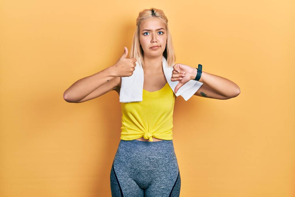 Beautiful blonde sports woman wearing workout outfit doing thumbs up and down, disagreement and agreement expression. crazy conflict  - Фото, изображение