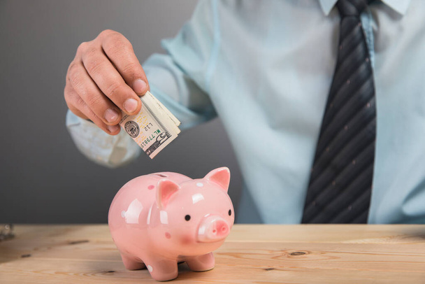 um homem coloca dinheiro em um banco porquinho - Foto, Imagem