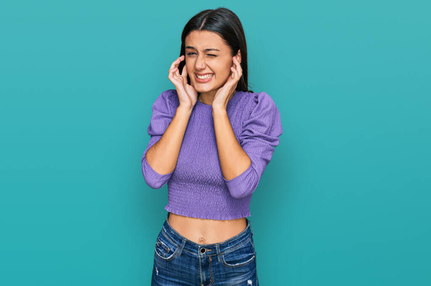 Young hispanic girl wearing casual clothes covering ears with fingers with annoyed expression for the noise of loud music. deaf concept.  - Photo, image