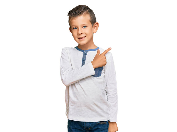 Roztomilé bělošské dítě v neformálním oblečení veselé s úsměvem tváře ukazující rukou a prstem na stranu se šťastným a přirozeným výrazem na tváři  - Fotografie, Obrázek