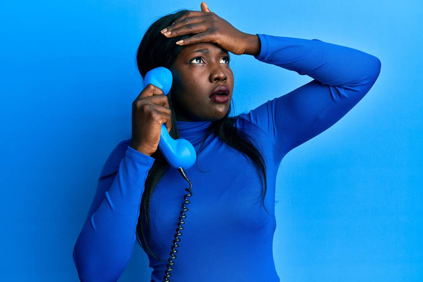 Jeune femme africaine parlant sur téléphone vintage stressé et frustré avec la main sur la tête, visage surpris et en colère  - Photo, image