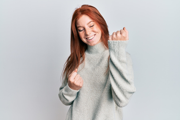 Joven chica pelirroja con suéter de invierno casual celebrando sorprendido y sorprendido por el éxito con los brazos levantados y los ojos cerrados  - Foto, Imagen