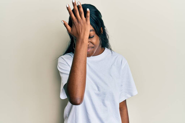Junge afrikanisch-amerikanische Frau trägt legeres weißes T-Shirt überrascht mit Hand auf Kopf für Fehler, erinnere dich an Fehler. Vergessenes, schlechtes Gedächtnis.  - Foto, Bild