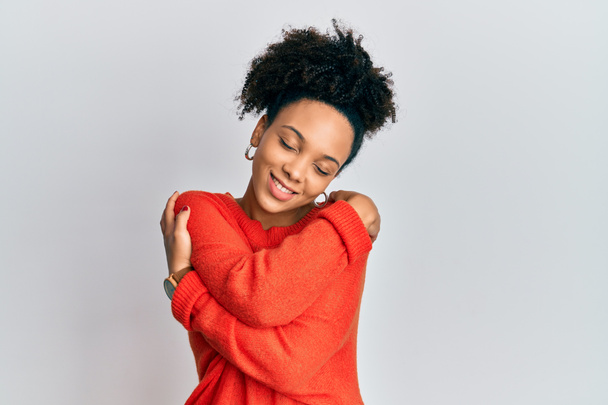Молода афроамериканка, одягнена в повсякденний одяг, обнімає себе щасливим і позитивним, усміхаючись впевнено. Любов і турбота про себе  - Фото, зображення