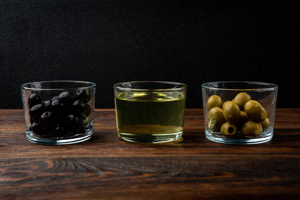 Vihreät ja mustat oliivit ja oliiviöljy tummalla puupohjalla. - Valokuva, kuva