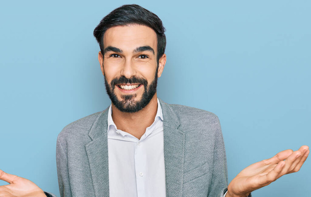 Jeune homme hispanique portant des vêtements de travail souriant montrant les paumes ouvertes des deux mains, présentant et comparant la publicité et l'équilibre  - Photo, image