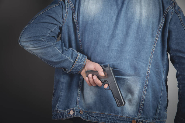 Ένας άνδρας κρατώντας ένα μαύρο πιστόλι στο χέρι του απειλεί - Φωτογραφία, εικόνα