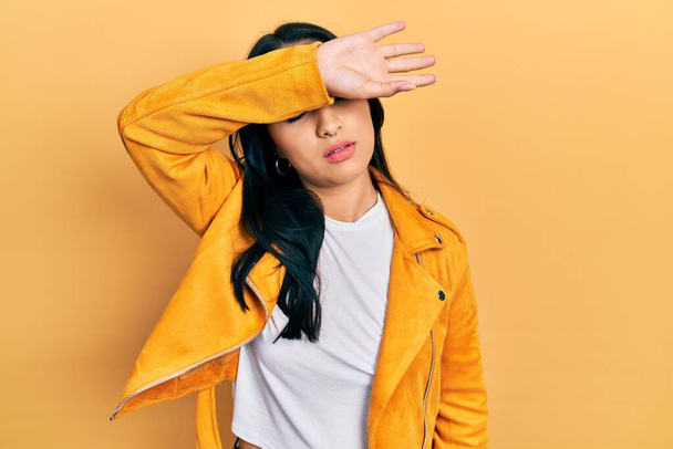 Beautiful hispanic woman with nose piercing wearing yellow leather jacket covering eyes with arm, looking serious and sad. sightless, hiding and rejection concept  - Photo, Image