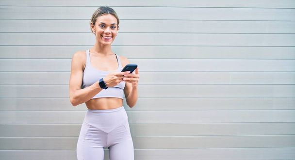 Jonge blanke fitnessvrouw draagt sportkleding training buiten met smartphone - Foto, afbeelding