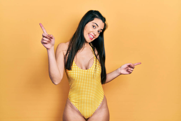 Fiatal spanyol lány fürdőruhát visel, magabiztosan mosolyog, ujjal mutogatva a különböző irányokra. hirdetési hely másolása  - Fotó, kép