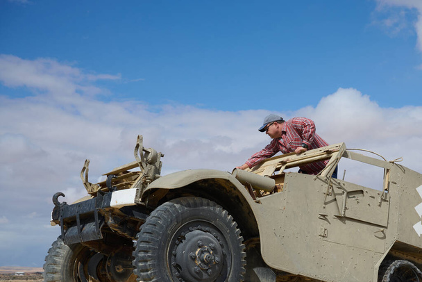 Egy férfi baseball sapkát és sötét szemüveget visel egy régi katonai járműben Nitzanban, Negevben.. - Fotó, kép