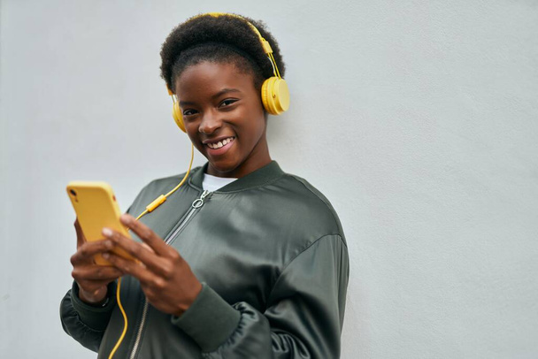 Jovem afro-americana sorrindo feliz usando smartphone e fones de ouvido na cidade - Foto, Imagem