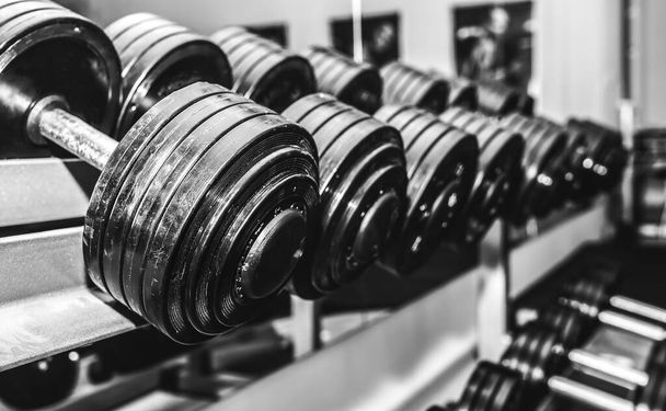 Heavy dumbbells lying in the raw in the gym. Fitness sport motivation. Happy healthy lifestyle living. Exercises with bars weights. Black and white photo. - Foto, Imagen