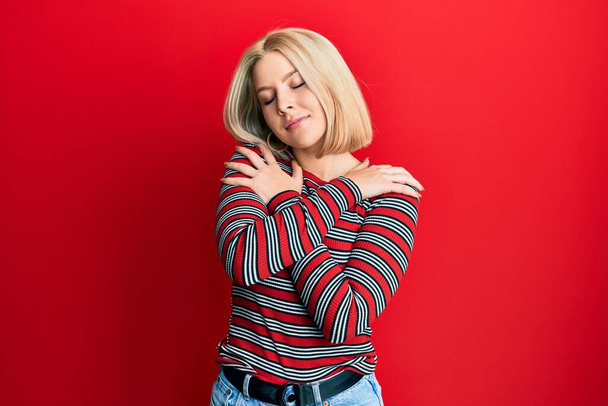 Nuori blondi nainen yllään rento vaatteita halaamalla itseään onnellinen ja positiivinen, hymyillen luottavainen. itserakkaus ja itsehoito  - Valokuva, kuva