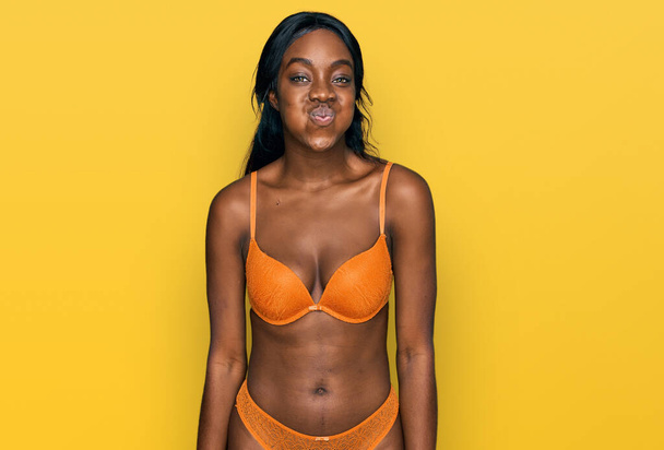 Jeune femme afro-américaine portant une lingerie gonflant les joues avec un drôle de visage. bouche gonflée d'air, expression folle.  - Photo, image