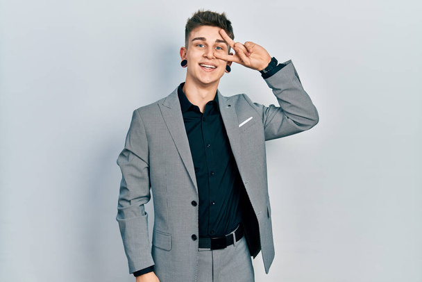 Young caucasian boy with ears dilation wearing business jacket doing peace symbol with fingers over face, smiling cheerful showing victory  - Photo, Image