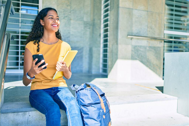 Молода афроамериканська студентка, користуючись смартфоном, сидить на сходах університету.. - Фото, зображення