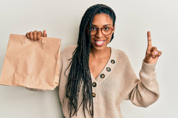 Afrikkalainen amerikkalainen nainen tilalla ottaa pois paperipussi hymyillen idea tai kysymys sormella onnellinen kasvot, numero yksi  - Valokuva, kuva
