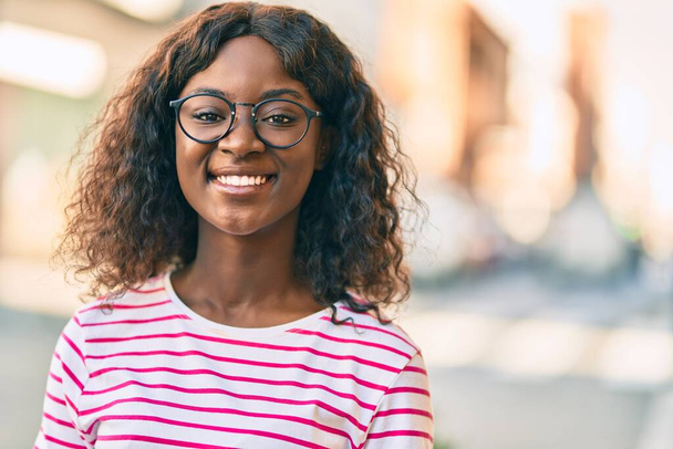 Joven afroamericana americana sonriendo feliz de pie en la ciudad. - Foto, Imagen