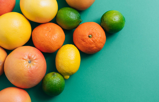 コピースペースのある緑のテーブルの上の柑橘類。ライム、レモン、オレンジ、イエローグレープフルーツ、ピンクグレープフルーツ、みかんなどの新鮮な柑橘類を緑の背景に空のスペースで縁取り - 写真・画像
