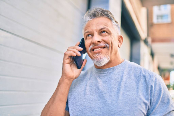 Mittelalter hispanischen grauhaarigen Mann lächelt glücklich reden auf dem Smartphone in der Stadt. - Foto, Bild
