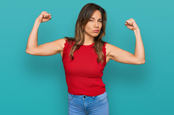 Mujer hispana joven vestida con ropa casual mostrando los músculos de los brazos sonriendo orgullosa. concepto de fitness.  - Foto, Imagen