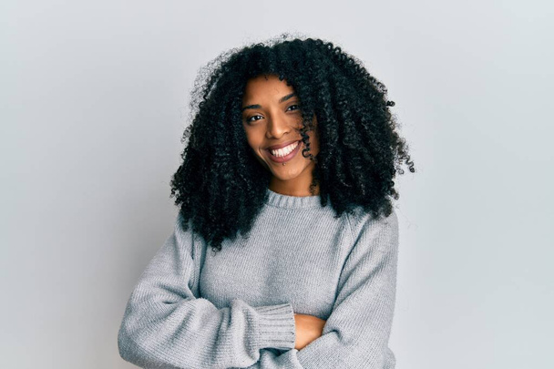 Mujer afroamericana con pelo afro vistiendo suéter casual de invierno cara feliz sonriendo con los brazos cruzados mirando a la cámara. persona positiva.  - Foto, imagen