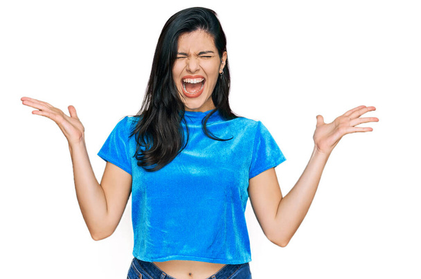 Νεαρή ισπανόφωνη γυναίκα φορώντας καθημερινά ρούχα γιορτάζει τρελός και τρελός για την επιτυχία με τα χέρια ψηλά και κλειστά μάτια ουρλιάζοντας ενθουσιασμένος. έννοια νικητή  - Φωτογραφία, εικόνα