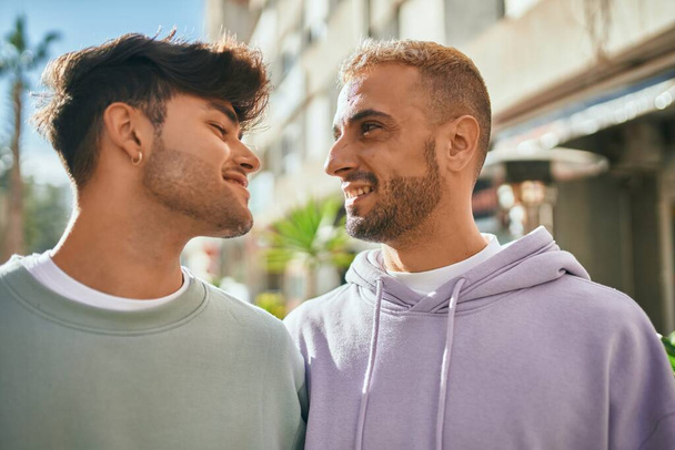 Νεαρό γκέι ζευγάρι χαμογελά χαρούμενο και αγκαλιάζει την πόλη. - Φωτογραφία, εικόνα