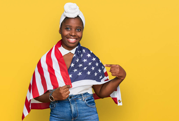 Jeune femme africaine avec turban tenant drapeau des États-Unis souriant heureux pointant avec la main et le doigt  - Photo, image