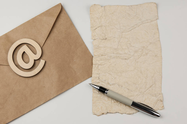 Sähköpostimerkki ruskeassa kirjekuoressa, jossa on tyhjä rypistynyt vanha paperiarkki, on valkoisella taustalla. Konsepti sähköpostiviesti kirje. Yläkuva - Valokuva, kuva