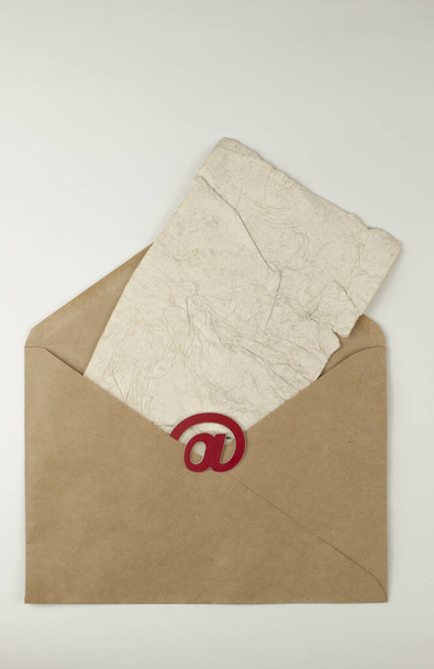 Sähköpostimerkki ruskeassa kirjekuoressa, jossa on tyhjä rypistynyt vanha paperiarkki, on valkoisella taustalla. Konsepti sähköpostiviesti kirje. Yläkuva - Valokuva, kuva