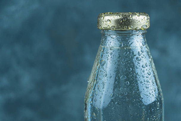 Botella de agua de vidrio con tapa dorada sobre fondo oscuro. Apaga tu sed con bebida fresca. Copiar espacio para texto - Foto, Imagen