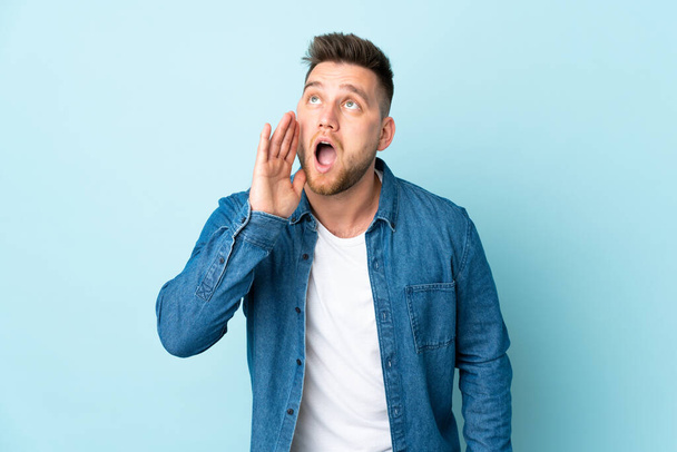 Russian handsome man isolated on blue background shouting with mouth wide open to the side - Photo, Image