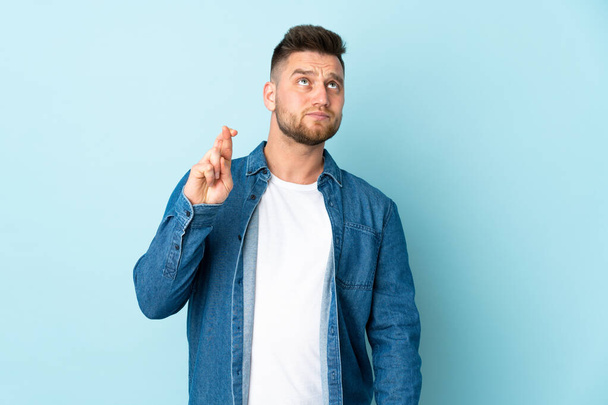 Russian handsome man isolated on blue background with fingers crossing and wishing the best - Foto, Imagen