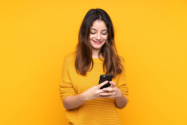Νεαρή καυκάσια γυναίκα απομονωμένη σε κίτρινο φόντο στέλνοντας μήνυμα με το κινητό - Φωτογραφία, εικόνα