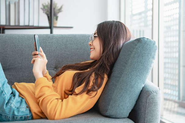 Femme heureuse utilisant un téléphone mobile sur le canapé à la maison. - Photo, image