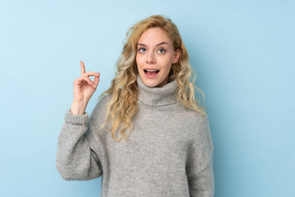 Young blonde woman wearing a sweater isolated on blue background intending to realizes the solution while lifting a finger up - Fotografie, Obrázek