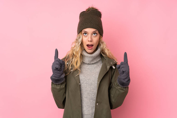 Kış şapkalı genç kız pembe arka planda izole edilmiş işaret parmağıyla işaret etmek harika bir fikir. - Fotoğraf, Görsel