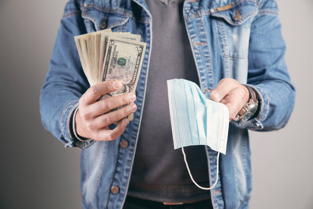 молодой человек держит медицинскую маску и деньги - Фото, изображение