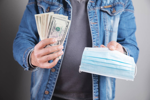 молодой человек держит медицинскую маску и деньги - Фото, изображение
