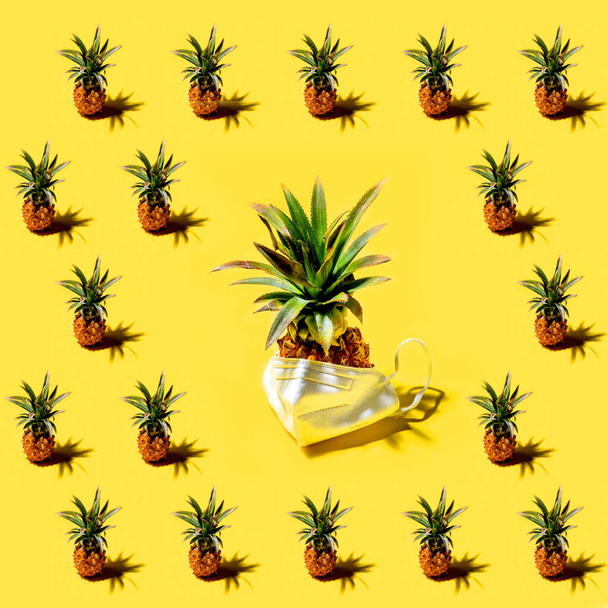 Fresh mini pineapples ananases and pineapples in medicine respirator mask with shadows on a bright solid yellow background pattern. Tropical style, summer pandemic vacation or illness concept. - Fotoğraf, Görsel