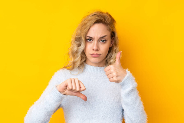 Young blonde woman isolated on yellow background making good-bad sign. Undecided between yes or not - Foto, imagen