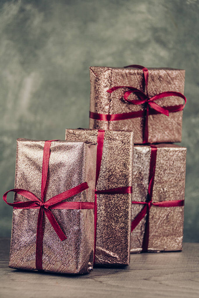 Групповые розовые коробки готовятся к празднику. Подарки на столе для подарков на вечеринке. Фольга блестит и повязана красной лентой - Фото, изображение