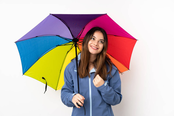Frau hält einen Regenschirm isoliert auf weißem Hintergrund, lacht und blickt auf - Foto, Bild