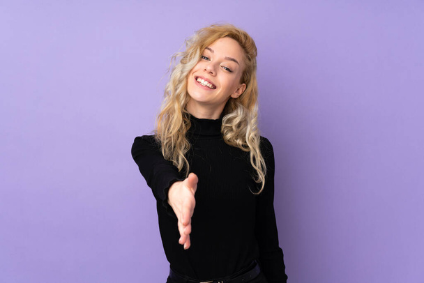 Молодая блондинка, изолированная на фиолетовом фоне, пожимает руки, чтобы заключить хорошую сделку - Фото, изображение