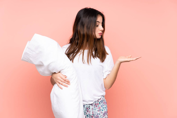Young woman in pajamas isolated on pink background holding copyspace imaginary on the palm - Foto, imagen
